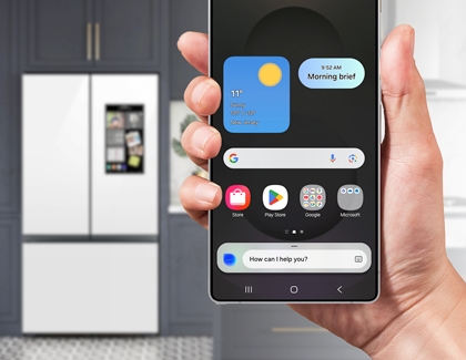 Galaxy S25 Ultra displaying the home screen with Bixby Voice wake-up activated, held in a hand, with a smart refrigerator in the background.