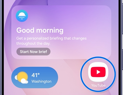 A Galaxy S26 screen showing a home page with the YouTube app icon highlighted in a blue circle.