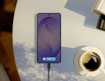 A purple Galaxy S26 Ultra on a white table, connected to a black charging cable, showing a full battery.