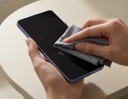 A hand wiping the Galaxy phone screen using a soft and dry cloth.