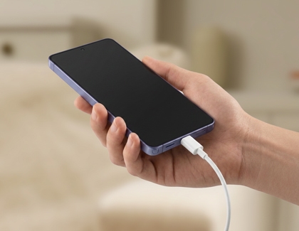 A hand holding a Galaxy phone while plugging in a charger.