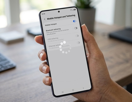 A hand holding a Galaxy phone showing the Mobile Hotspot and Tethering settings screen with a loading indicator on the display.