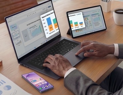 A purple Galaxy S26 Ultra on a desk next to a person using a laptop and tablet that are syncing data and charts.