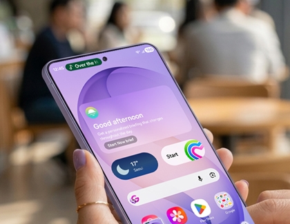 A hand holding a Galaxy S26 Ultra showing the home screen with widgets and status bar icons.