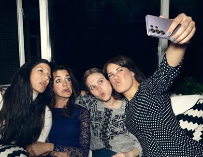 Four friends making funny faces while one holds up a purple Galaxy S26 Ultra to take a group selfie at night.