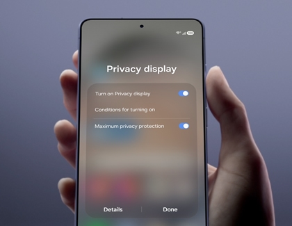 A hand holding a Galaxy S26 Ultra showing the Privacy display settings menu with two blue toggle switches turned on.