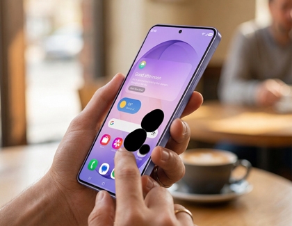 A hand holding a Galaxy phone showing a large black ink spot on the screen.