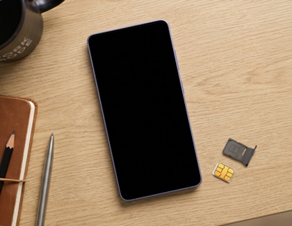 A Galaxy phone lying flat on a wooden desk next to a removed SIM tray and SIM card.
