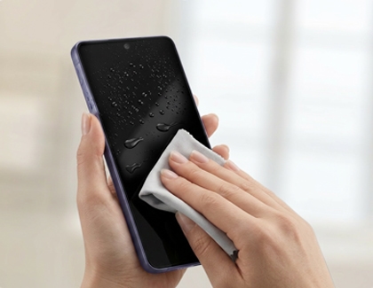 Using a dry microfiber cloth to wipe water droplets off a Galaxy phone screen.