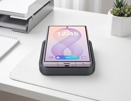 A silver Galaxy Z Fold8 Ultra displayed on a wireless charging pad placed on a white desk showing the lock screen.