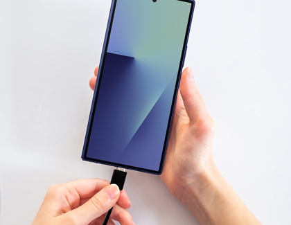 Person plugging a USB-C cable into the bottom of a Galaxy phone against a white background.