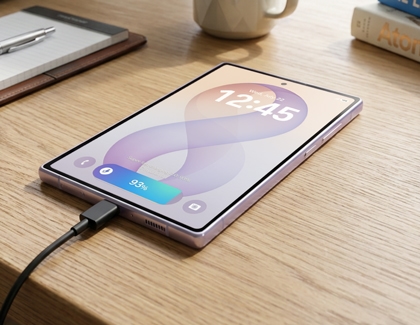 A silver Galaxy Z Fold8 Ultra displayed on a wooden desk showing the lock screen with a charger connected at the bottom.