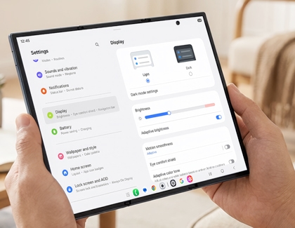 Hands holding the unfolded Galaxy Z TriFold displaying the Display settings menu with Light mode selected.