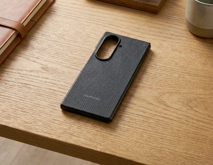 Black textured Galaxy Z TriFold case on a wooden table next to a brown notebook.