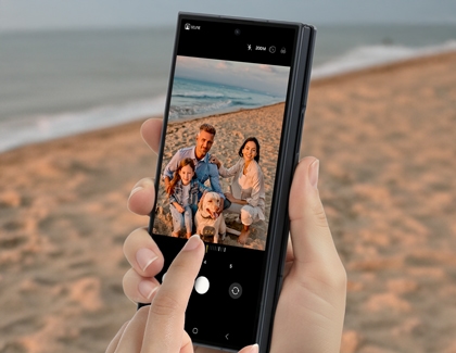 Hands holding the Galaxy Z TriFold cover screen showing the camera interface with a finger touching the zoom bar.