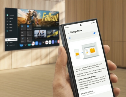 Hand holding a Galaxy Z TriFold showing Storage Share settings in front of a television displaying a movie menu.