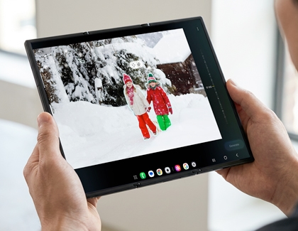 Hands holding the unfolded Galaxy Z TriFold displaying a photo of two children in the snow with white outlines around them.