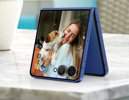 Galaxy Z Flip7 placed on a table in FlexCam mode, showing a selfie preview with a woman and a dog.