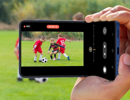 Person using the Galaxy Z Flip7 in Camcorder mode to record children playing soccer on a grassy field.