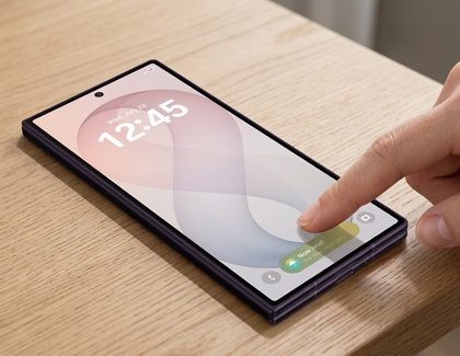 A hand touching the cover screen of a folded Galaxy Z Fold device resting on a wooden table.
