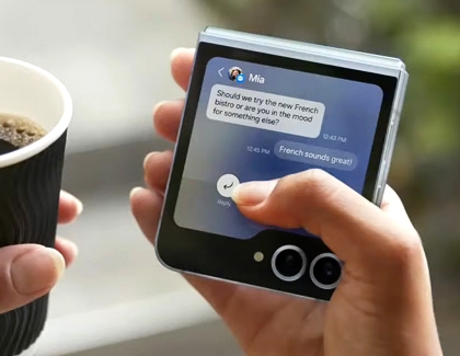 A Woman holding coffee in one hand and a Galaxy Z Flip6 in another hand while responding to a message using the cover screen