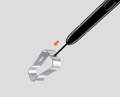 A close-up of an S Pen with its tip inserted into a metal clip tool for nib replacement, indicated by a red arrow.