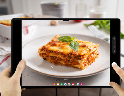 A person using a Galaxy tablet to take a picture of lasagna while using Food mode