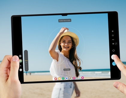 A person using a Galaxy tablet to take a portrait video of a women wearing a beach hat