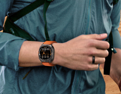 Close-up of a person wearing an orange-banded Galaxy Watch Ultra on their wrist while also wearing a Galaxy Ring on their finger.