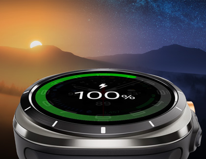 A Galaxy Watch7 with a fully charged battery indicator against a scenic background of a sunrise over mountains.