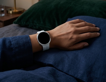 A Galaxy watch being worn on a wrist resting on a bed.