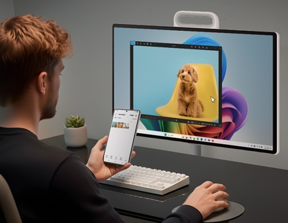 Person holding a smartphone while using Samsung MovingStyle display showing an image editing window with a dog.