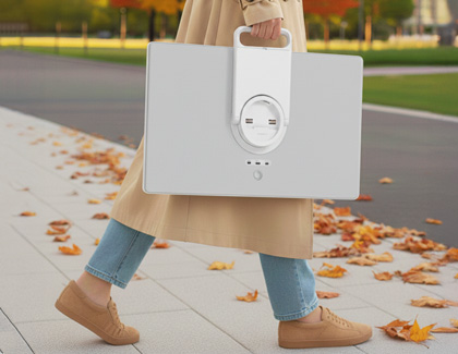 Person in a tan trench coat and jeans carrying the MovingStyle TV screen by its handle.