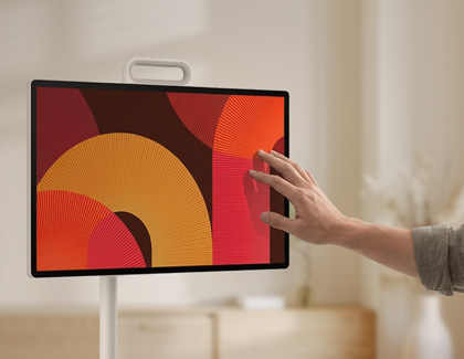 A hand reaching out to touch the screen of a MovingStyle on a white floor stand.