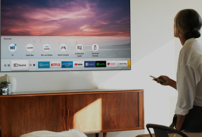 Woman standing in front of a Samsung TV, pointing a remote at it