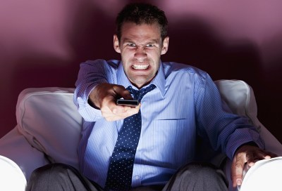 Man watching TV and holding remote, frustrated that the sound is dropping out