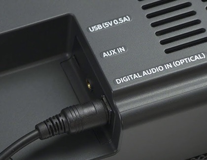 Close-up of a Samsung soundbar showing a cable connected to the AUX IN port, with labels for USB and Digital Audio IN (Optical).
