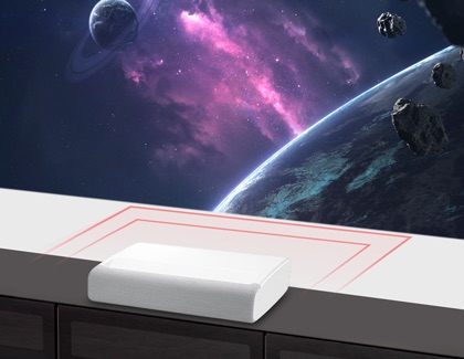 Samsung Premiere projector placed on a cabinet projecting a space scene with planets and asteroids on the wall.