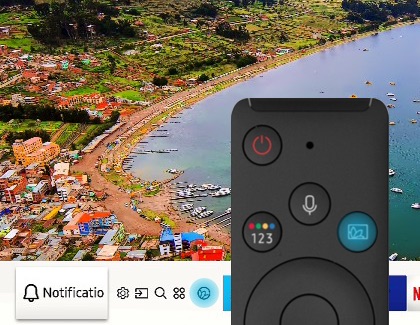 Samsung TV remote with the Ambient Mode button highlighted against a TV screen displaying a scenic shoreline.