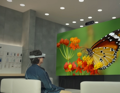 A person seated and watching a large virtual butterfly display while wearing the Galaxy XR headset.