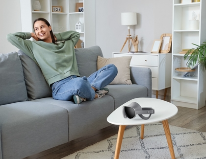 A person relaxing on a couch with the Galaxy XR headset resting on a nearby table.