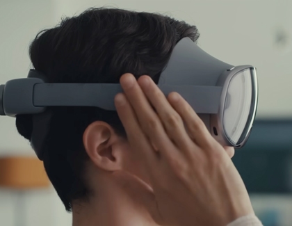 A person wearing the Galaxy XR headset and raising a hand near the side to enable Passthrough.