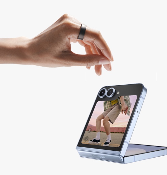A hand wearing Galaxy Ring can be seen, making a pinching motion. A closed Galaxy Z Flip6 with the camera open on the cover screen can be seen. Above the smartphone are two icons: Camera and Turn off alarms.