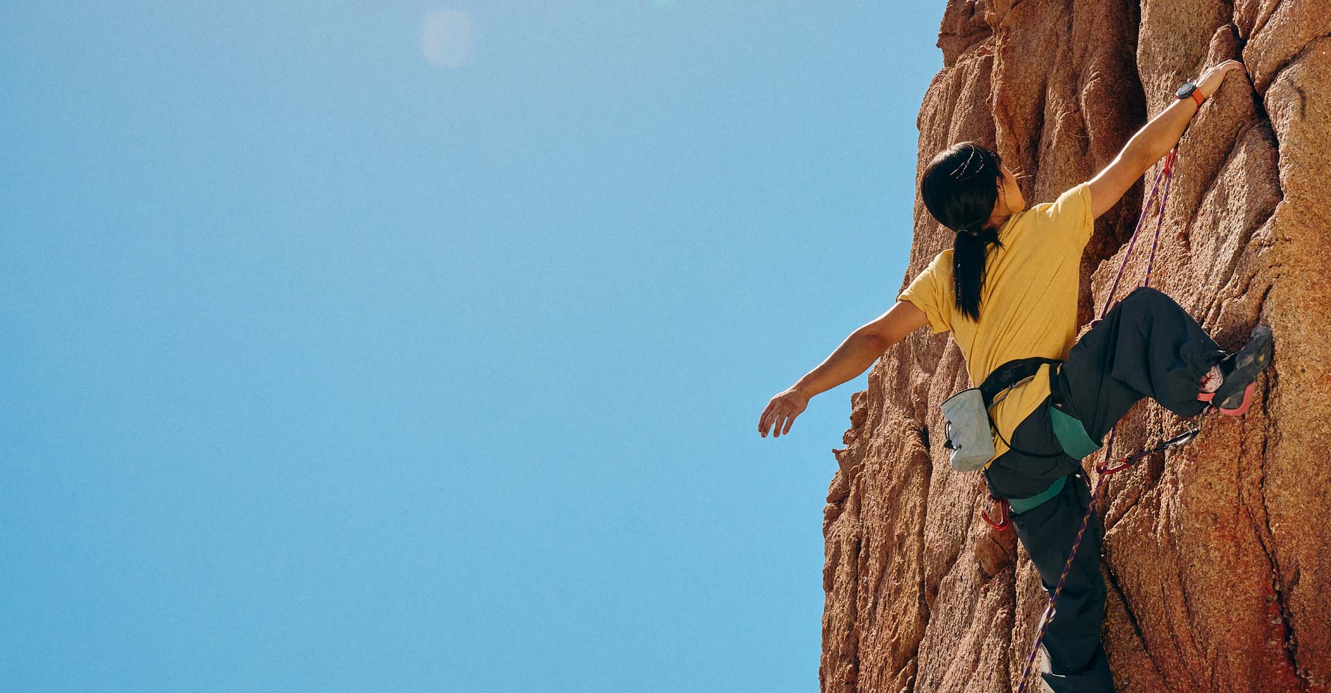 A woman is rock climbing with a Galaxy Watch Ultra on her wrist.