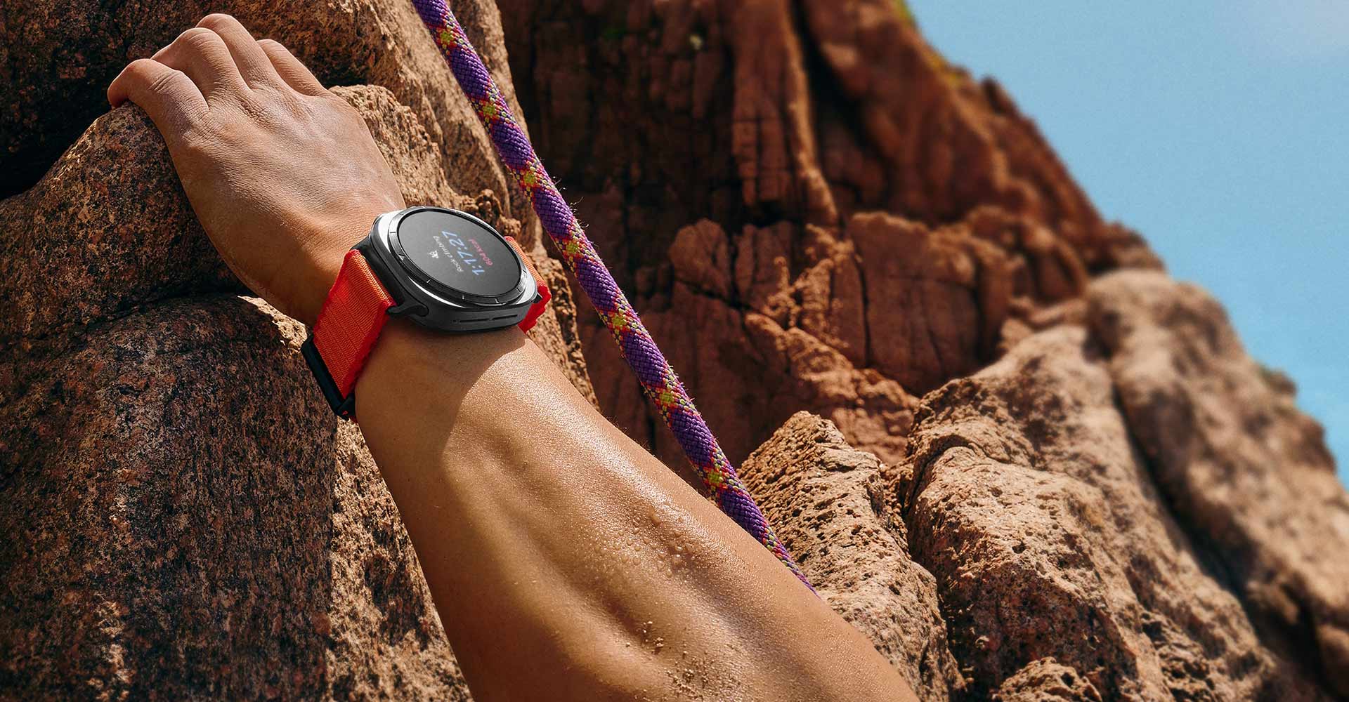 A hand grabbing a rock on the mountain is wearing a Galaxy Watch Ultra on the wrist.