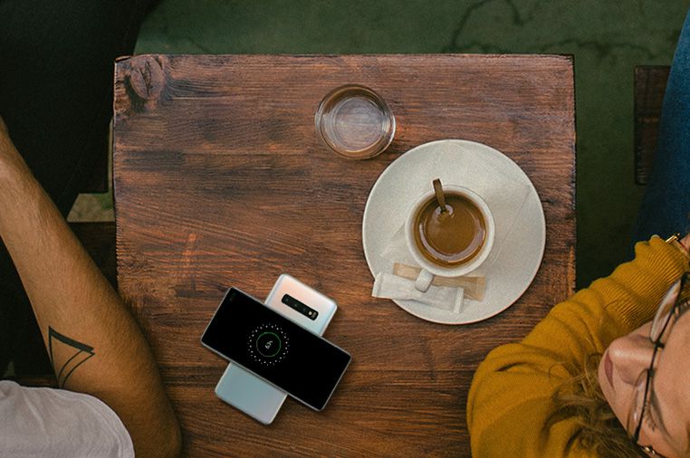 Samsung Galaxy S10 Featuring Wireless PowerShare - Table in Coffee Shop with Man and Woman Charging S10 using Another S10