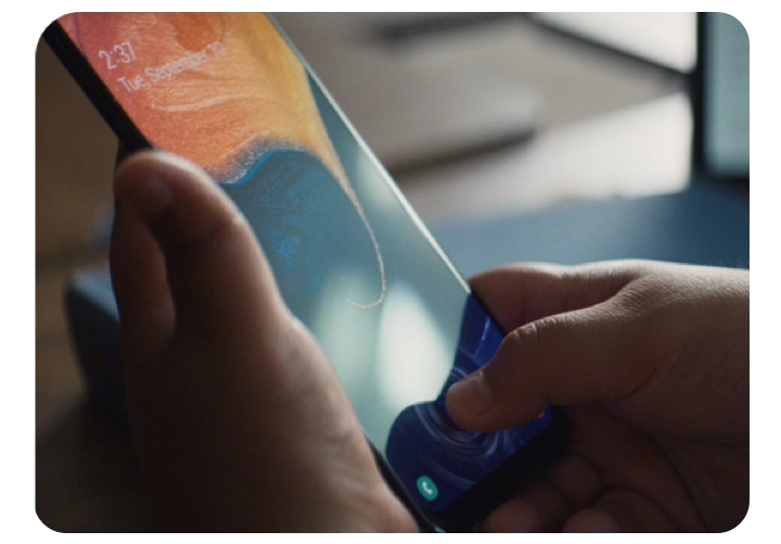 A close up pair of hands. One hand is holding an A-Series phone at a 75-degree angle while the other is tapping a bottom button on the phone. 