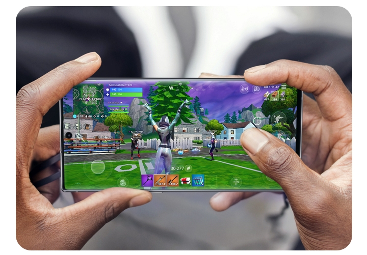 Close up pair of hands holding a Galaxy 5G phone in landscape orientation playing Fortnite. 