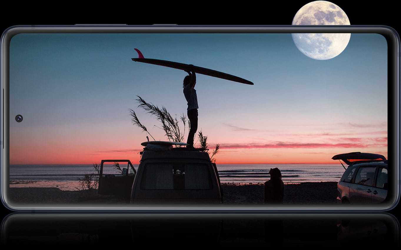 Galaxy S20 FE 5G with a nighttime photo onscreen showing a shadow of a person holding a surfboard above their head. Above is a full moon in the sky. The full moon is half outside of the screen, representing the all-day battery life available on Galaxy S20 FE 5G. 