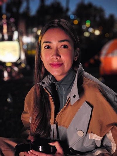 Nightography portrait photo of a woman sitting outside at a camp ground. String lights faintly …